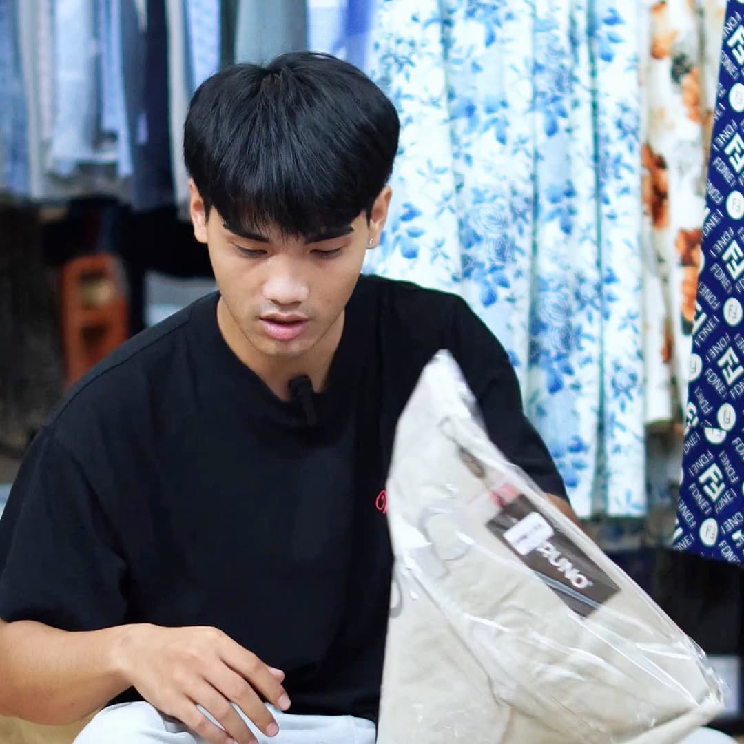 Nhân viên shop thời trang ngồi cầm từng túi quần áo lên, tìm tem trên từng chiếc