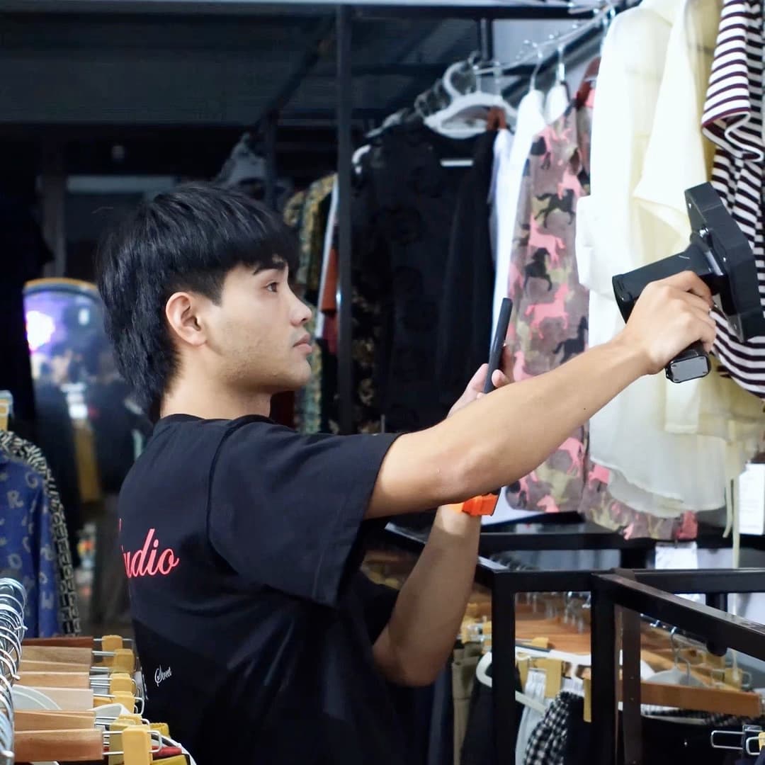 Nhân viên shop cầm máy đọc RFID cầm tay của Nextwaves quét dọc sào quần áo treo