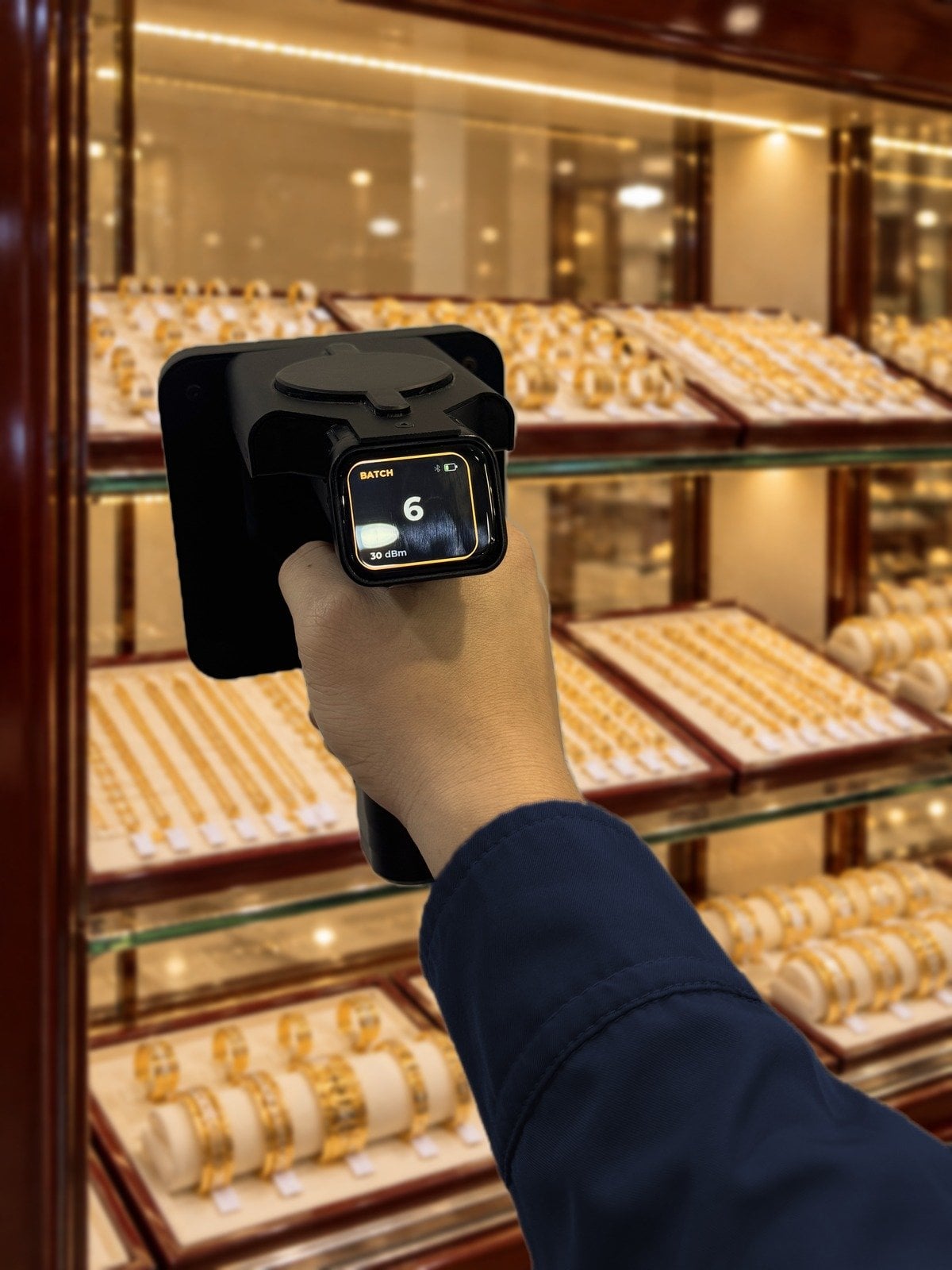 Hình minh hoạ: cầm máy quét RFID cầm tay Nextwaves quét các khay vàng trong tủ trưng bày đã mở