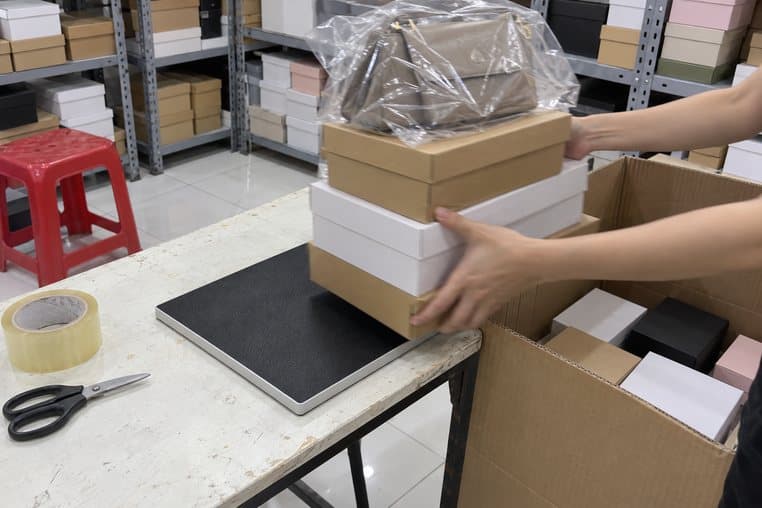 Hình minh hoạ: nhấc chồng hộp giày và túi xách đã soát trên đầu đọc RFID để bàn vào thùng chuyển hàng