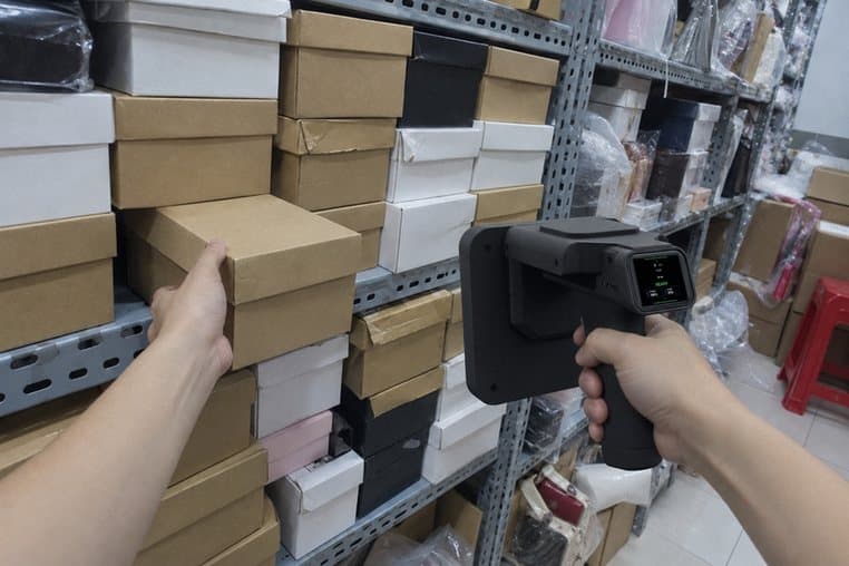 Hình minh hoạ: máy quét RFID dò ra đúng hộp giày, tay rút hộp đó khỏi kệ