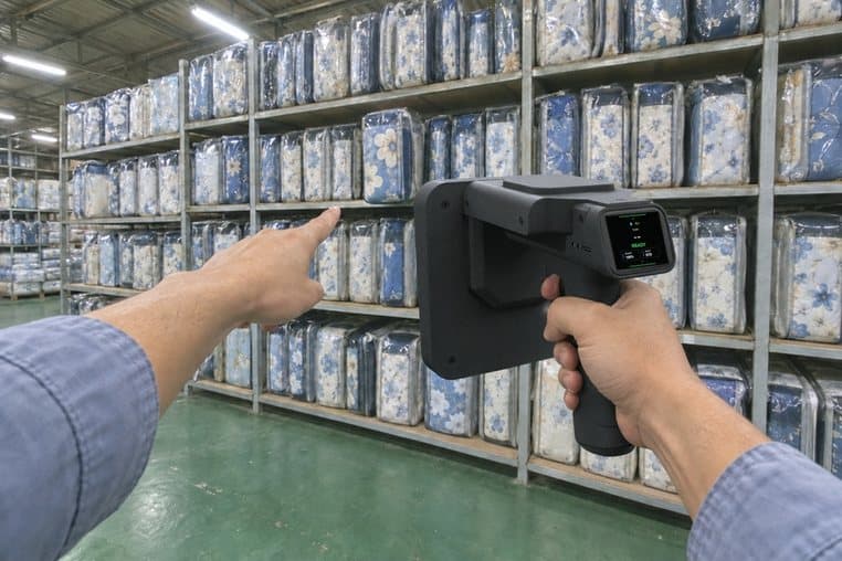 Hình minh hoạ: đứng xa chĩa máy quét RFID vào cả kệ chăn ga giống nhau, tay chỉ vào đúng túi vừa dò ra